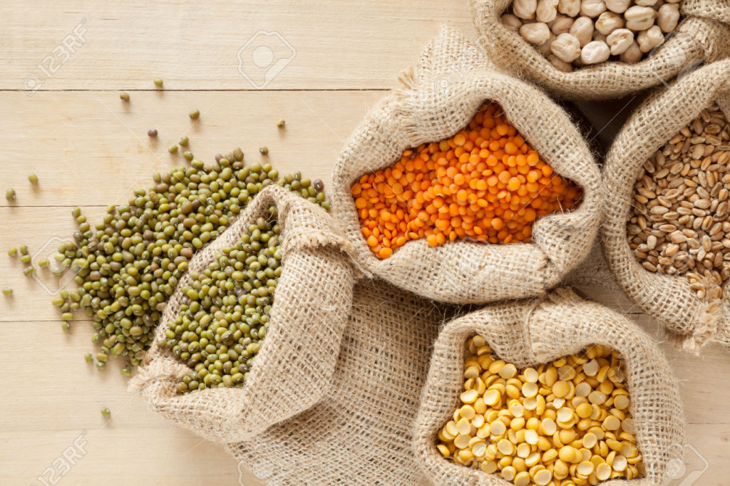 bags with cereal grains: red lentils, peas, chick peas, wheat and green mung on wooden table