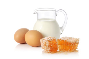 Glass jug with milk, two eggs and yellow honeycomb on white background